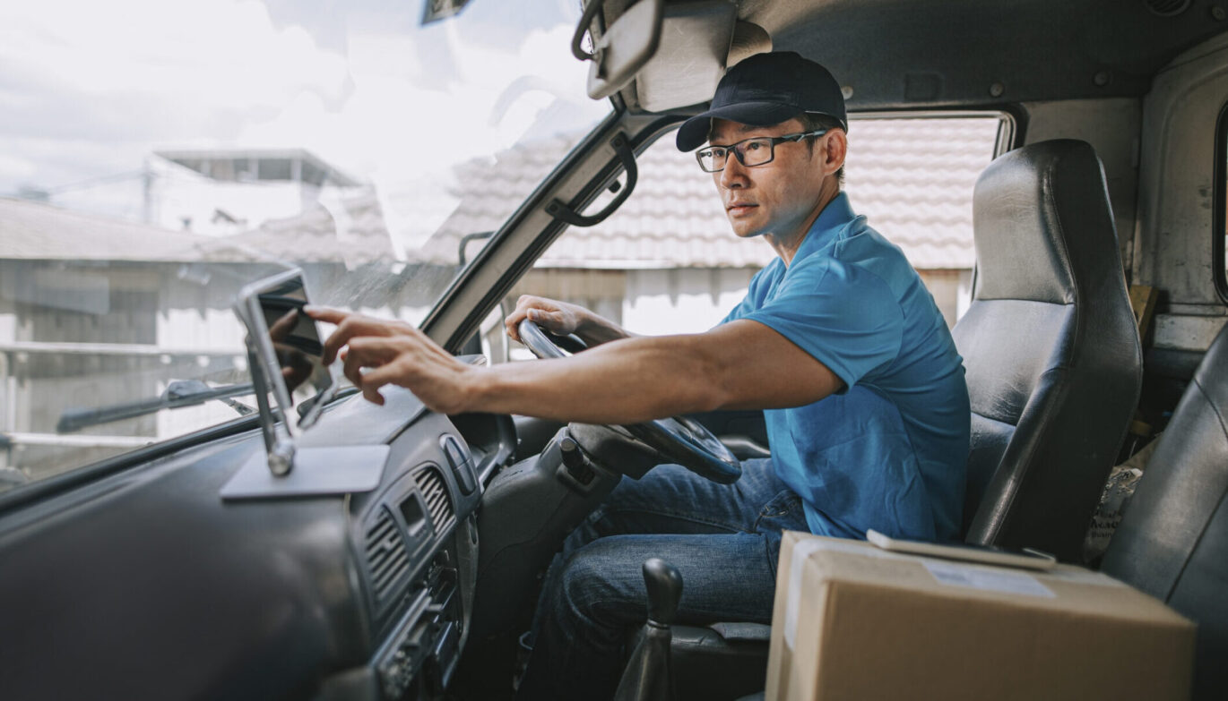 asian chinese mature male delivery person using digital tablet mobile app checking delivery information in driver’s seat in delivery van